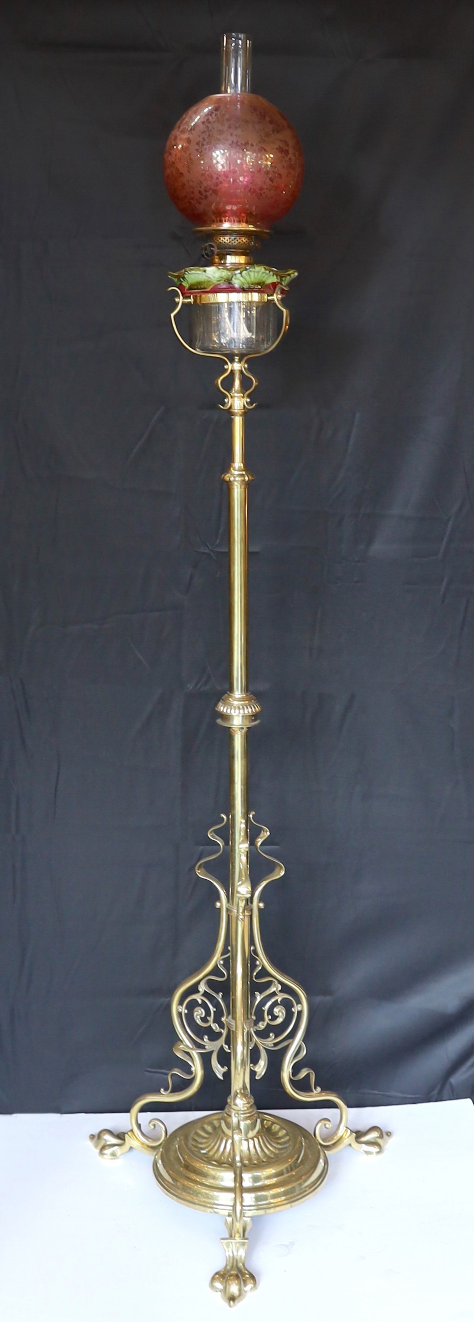 An Edwardian brass telescopic oil lamp standard, with later edged cranberry glass shade and duplex mechanism, height 168cm. width 52cm